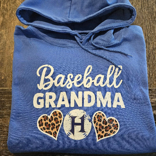 Blue hoodie with 'Baseball Grandma' text and heart designs on a wooden surface